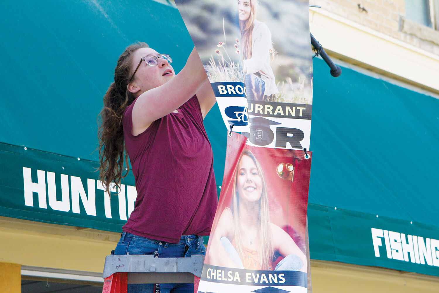 Kate Norman hangs a banner celebrating BHS Seniors on Main Street